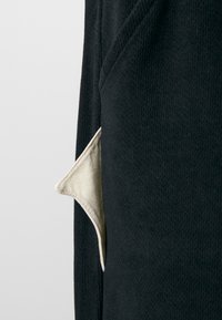 Black textured fabric with a visible white cotton pocket detail. The pocket has a triangular shape and contrasts with the surrounding material.