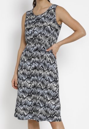 Robe sans manches, longueur genou, avec un motif abstrait noir et blanc rappelant des plumes, portée par une personne avec une main sur la hanche et l'autre détendue.