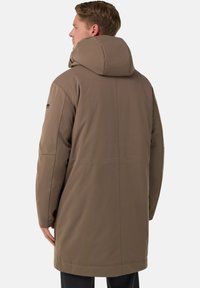 Brun vadderad rock med stor huva, slät yta, rak skärning och minimala sömnadsdetaljer. Bakifrån syns rena linjer och modern design.