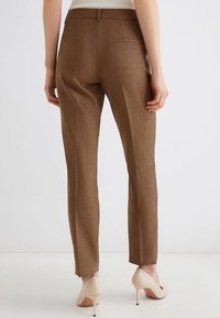 Pantaloni a scacchi marroni con una vestibilità su misura, dotati di tasche posteriori e una texture liscia. Indossati con tacchi alti beige.