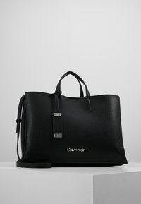 Czarna skórzana torba na ramię o teksturowanym wykończeniu, z podwójnymi uchwytami, odpinanym paskiem, srebrnym okuciem oraz wytłoczonym logo "Calvin Klein" z przodu.