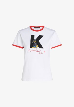 Camiseta de algodón blanca con cuello y dobladillos de mangas rojos. Presenta un gráfico de un 'K' negro y Pato Donald con una firma en rojo.