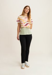 T-shirt accorciato a righe multicolori (giallo, rosa, viola) con una base verde. Abbinate a pantaloni neri e sneakers argentate.