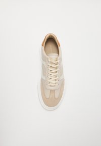 Baskets beiges avec tige en cuir et daim, semelle blanche, bout rond et lacets beiges. Logo sur la languette et accent de talon beige.