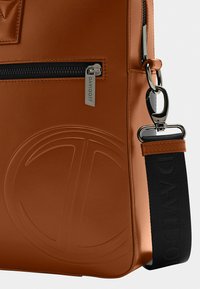 Brown leather shoulder bag with a textured finish, featuring a zippered pocket and branded hardware. Black strap with embossed logo detail.