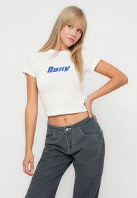 White cropped t-shirt with blue "Roxy" logo, paired with gray wide-leg pants featuring front pockets and stitched detailing.