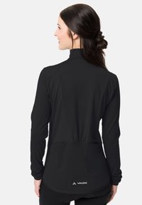 Čierna dlhá bunda s dlhým rukávom vyrobená z elastického materiálu, s vysokým golierom, priliehavým strihom a zadnými vreckami. Na dolnom leme sa nachádza logo.