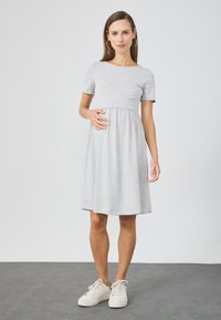 Harmaa lyhythihainen mekko, jossa on tiukka bodice ja virtaava hame, valmistettu pehmeästä kankaasta. Yhdistetty valkoisiin tennareihin. Yksinkertainen muotoilu, polvipituinen.