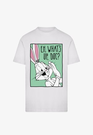 Bílé tričko s grafikou kresleného králíka s dlouhýma ušima a širokým úsměvem, který říká "HEJ, CO SE DĚJE, DOKTORE?" na zeleném pozadí.
