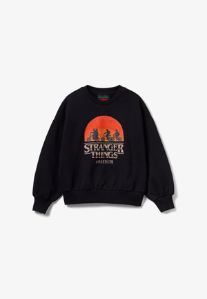 Sweatshirt noir avec un graphique de soleil rouge-orange, trois silhouettes à vélo, et le texte "Stranger Things" sur le devant.