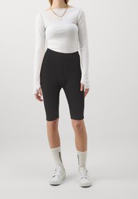 Svarta cykelshorts kombinerat med en figurnära, vit långärmad topp. Har en slank design, smidigt tyg och enkel silhuett. Bärs med vita sneakers.