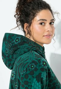 Zielona bluza z polaru z wzorem ciemnych kwiatów i zwierzęcych nadruków. Posiada zamek błyskawiczny i duży, usztywniany kaptur.