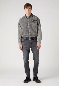Grijze denim overhemd met knoopsluiting en borstzak, gecombineerd met grijze jeans. Zwarte leren schoenen maken de outfit compleet. Eenvoudig, casual ontwerp.