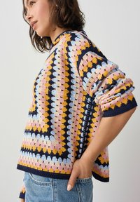 Kolorowy sweter na szydełku z geometrycznym wzorem w kolorach różowym, niebieskim, żółtym i granatowym. Długie rękawy z detalami mankietów i luźny krój.