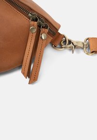 Bruine leren tas met twee ritsen, messing hardware, een afneembare schouderband en zichtbare stikdetails. Vlotte textuur en ronde vorm.