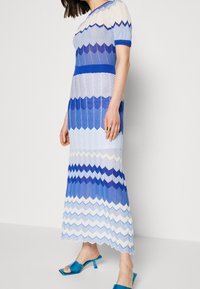 Robe longue à motif zigzag dans différentes nuances de bleu et blanc. Confectionnée en tissu léger avec des manches courtes et un col rond.