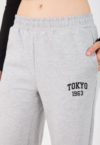 Szare dresy wykonane z miękkiego, teksturowanego materiału. Posiadają elastyczny pasek w talii oraz nadrukowany czarny wzór "TOKYO 1963" po boku.