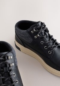 Čierne kožené poltopánky so sivým textilným golierom, kontrastnou bielou podrážkou, kovovými očkami a šnúrkami s textúrou.