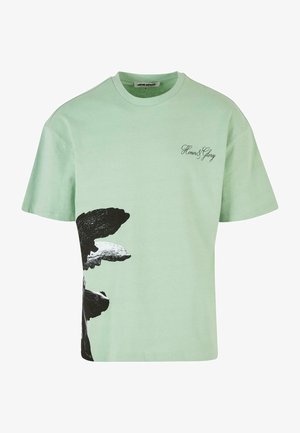 Camiseta de algodón verde menta con un estampado gráfico en blanco y negro en el costado y texto "Honor & Glory" en una fuente cursiva. Diseño de cuello redondo.