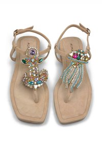 Sandali piatta beige con una striscia tra le dita. Gli abbellimenti decorativi includono gemme colorate che formano un design a ancora e medusa.