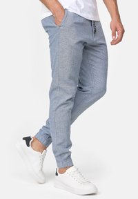 Helle blaue Jogginghosen aus strukturiertem Stoff, mit Seitentaschen, elastischen Bündchen und einer Kordelzugverschluss. Kombiniert mit weißen Turnschuhen.