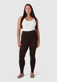 Leggings marroni a vita alta abbinati a un top bianco senza maniche. Materiale morbido ed elastico con una texture liscia. Design semplice, vestibilità a tutta lunghezza.