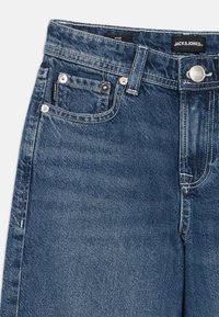 Τζιν παντελόνια σε σκούρο μπλε με σχεδιασμό φαρδιάς γραμμής. Διαθέτουν κλείσιμο με κουμπί, ασημένια μεταλλικά στοιχεία και μικρές μπροστινές τσέπες.