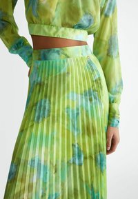 Gonna plissettata verde e top a maniche lunghe coordinato, realizzati in tessuto leggero con motivi ad acquerello astratti blu e verdi.