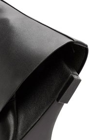 Sac à main en cuir noir avec une texture lisse, un design minimaliste et un accent matériel angulaire distinct à l'ouverture.