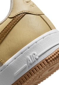 Gros plan sur le talon d'une basket beige avec des accents marron, une semelle intermédiaire blanche comportant le texte "AIR", et une semelle extérieure en caoutchouc texturée.
