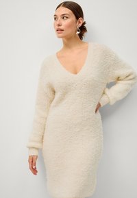 Vestito a maglia color crema con scollatura a V, design morbido, tessuto texturizzato e maniche lunghe, con polsini e orlo a costine.
