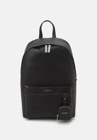 Black synthetic backpack with smooth texture, rounded shape, double zipper, front pocket, and attached small pouch. Calvin Klein logo visible.