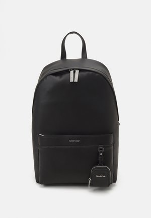 Zaino sintetico nero con texture liscia, forma arrotondata, doppia zip, tasca frontale e piccolo borsellino attaccato. Logo Calvin Klein visibile.