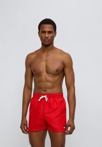 Κόκκινα μαγιό σορτς από ελαφρύ ύφασμα, με ρυθμιζόμενη μέση με κορδόνι, λευκή ραφή και μικρό λογότυπο στη αριστερή πλευρά.