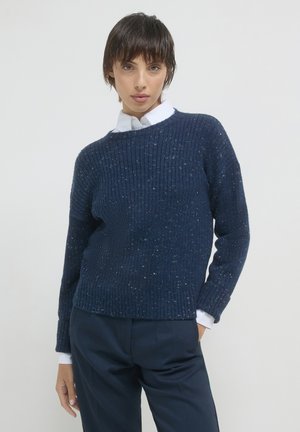 Maglione lavorato a maglia blu navy con texture a coste in rilievo, dettagli screziati, ampio scollo rotondo e maniche lunghe, abbinato a una camicia bianca con colletto.