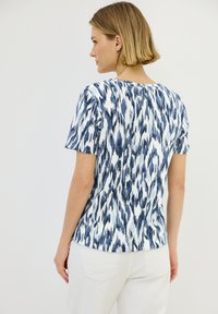 Camicia a maniche corte con un motivo astratto blu e bianco, con scollatura rotonda e vestibilità comoda. Realizzata in tessuto leggero.