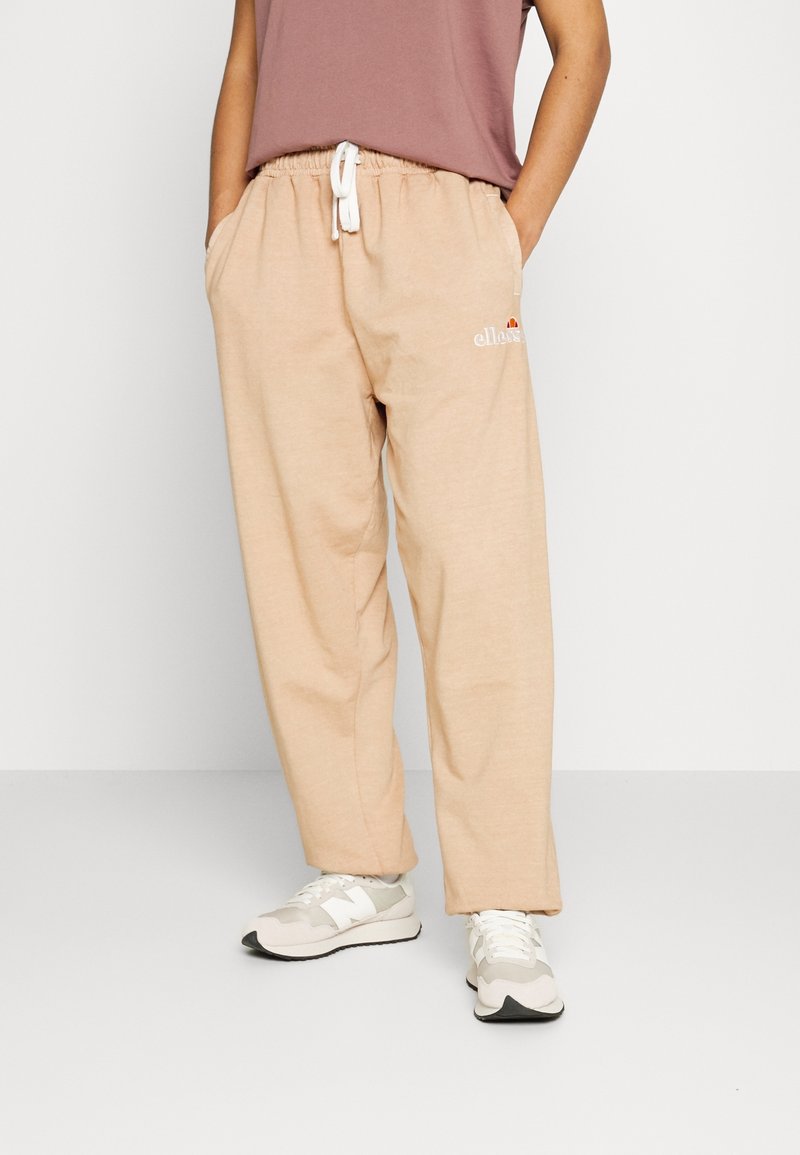 Beige sweatpants med elastisk midja och dragsko, med sidfickor och en liten logotyp på vänster ben. Stylad med en mauve skjorta.