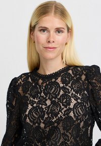 Černý krajkový top s květinovými vzory, zvlněným výstřihem a nabíranými rukávy s poloprůhlednou texturou. Elegantní design zdůrazňuje detaily.