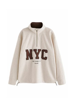 Beige fleece trui met een half-rits kraag, met "NYC" in donkerbruine letters en "New York City est. 1982" in kleinere tekst eronder.