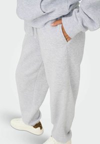 Lysgrå sweatpants med en afslappet pasform, der har sidelommer og en blød, tekstureret overflade. Parret med hvide sneakers med en leopardprint-detalje.