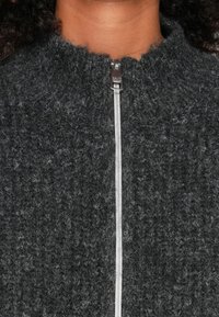 Suéter texturizado cinza em malha, com fecho éclair, apresentando um colarinho alto e um zíper prateado no centro, destacando um material suave e felpudo.