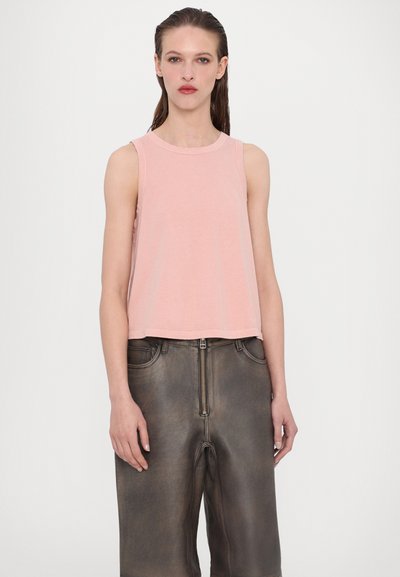 Top corto de color rosa claro con escote redondo y diseño sin mangas, combinado con pantalones de cuero marrón oscuro de tiro alto con cremallera en la parte delantera.