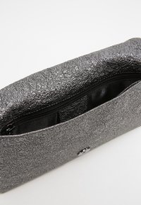 Clutch grigia metallica con superficie texturizzata, interno con zip e chiusura a bottone argentato lucido. Presenta una fodera nera e scomparti interni.