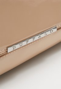 Beige lackläderhandväska med en silverfärgad metallplåt som har texten "BUFFALO" tydligt synlig på framsidan. Slät yta, enkel design.