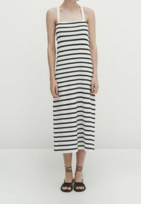 Robe midi à rayures noires et blanches avec un décolleté carré et de fines bretelles. Associée à des sandales noires à brides. Tissu en coton lisse.