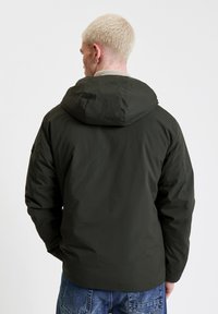 Giacca imbottita verde oliva con cappuccio, caratterizzata da una texture liscia e polsini elastici. La vista posteriore mostra un taglio dritto e un detailing minimale.