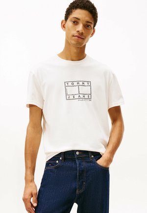 Witte katoenen t-shirt met het logo "TOMMY JEANS" in het zwart, gecombineerd met donkerblauwe denim jeans met een klassieke pasvorm en subtiele stikseldetails.