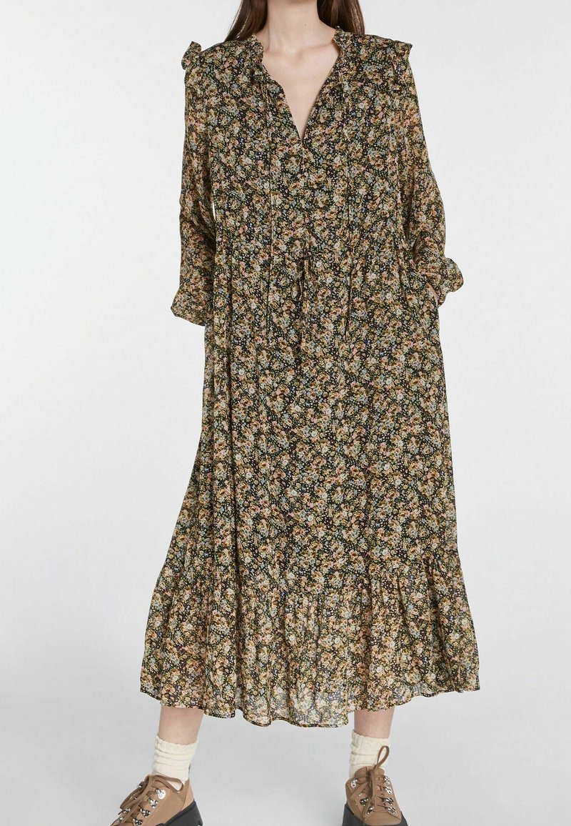 Robe midi fleurie en vert foncé avec col froncé et manches longues. Tissu léger avec jupe à volants et liens à la taille.