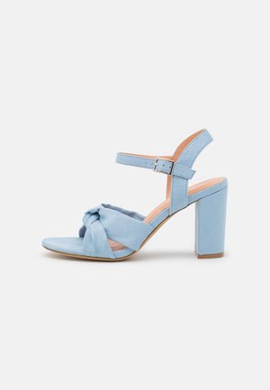 Lyseblå ruskind høje hæle sandal med ankelrem, spænde og snoet forside design på hvid baggrund.