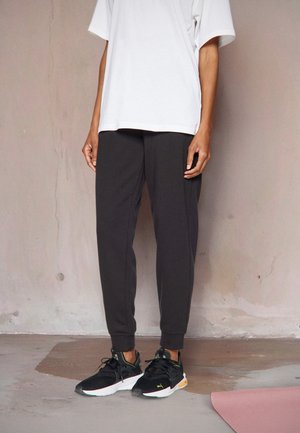 Svart joggebukse med tapered fit, sammen med en løs hvit t-skjorte og svarte joggesko med neonlys.